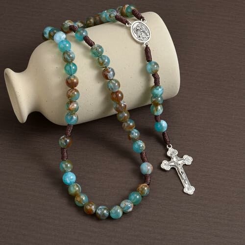 Rosary with blue and brown beads draped over a ceramic vase.