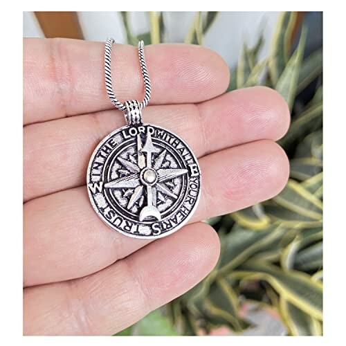 Hand holding compass pendant necklace with inscription