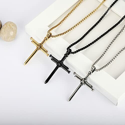 Three cross necklaces in gold, black, and silver on a white surface