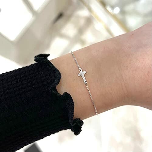 Silver cross bracelet on wrist with black sleeve