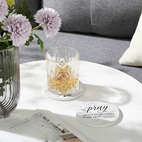 Crystal glass with drink on white table next to flowers and coasters.
