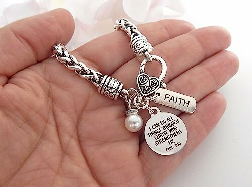 Hand holding a silver bracelet with faith charm and inspirational quote.