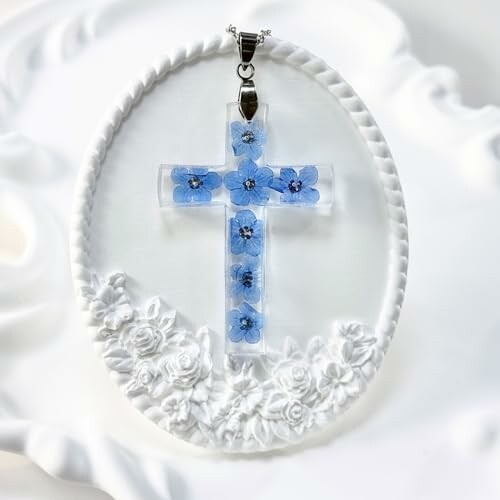 Cross pendant with embedded blue flowers on white background.