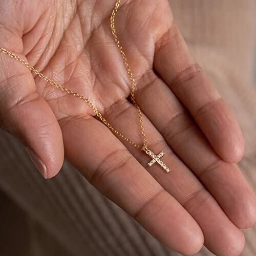 Hand holding a gold cross necklace.