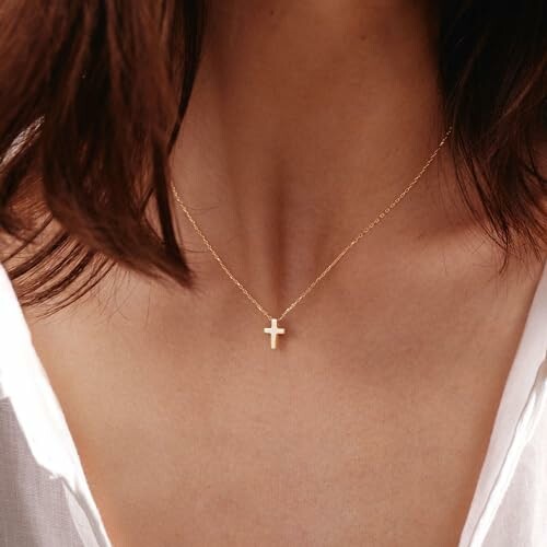 A woman wearing the HANLI Cross Necklace admires her reflection in a mirror, showcasing the necklace's elegant design.