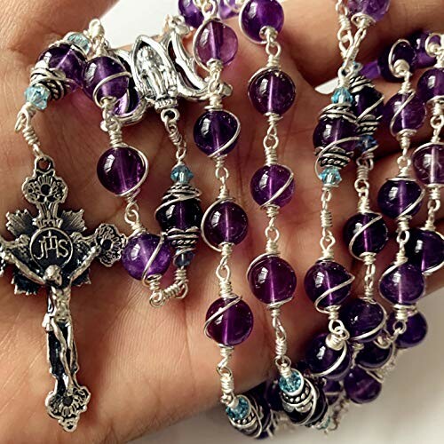 Hand holding a purple rosary with silver accents.