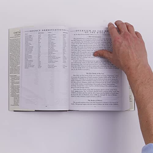 Hand turning a page in an open book on a white surface.