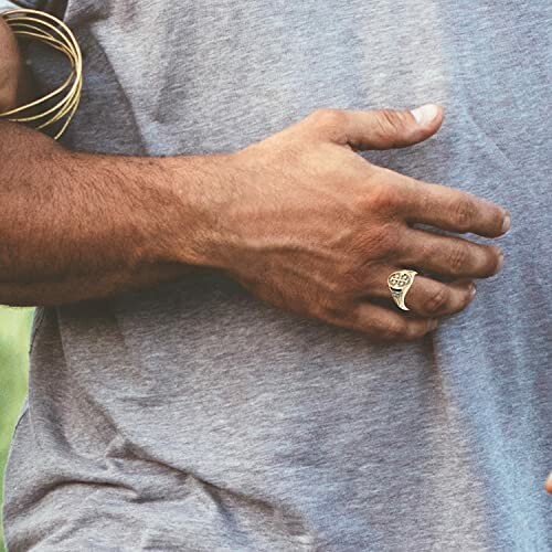 Man's hand wearing a gold ring on a gray shirt
