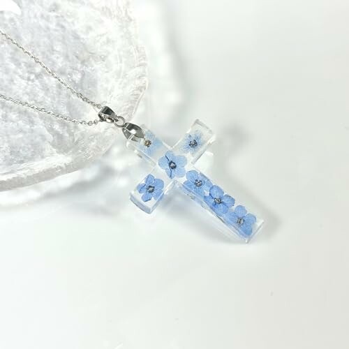 Clear resin cross pendant with embedded blue flowers on a silver chain.