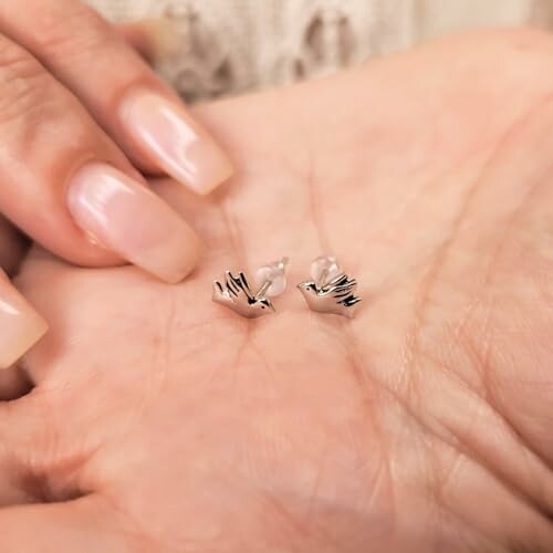 Hands holding small silver bird-shaped earrings