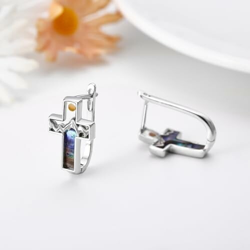 Silver cross earrings with decorative inlays on a white surface.