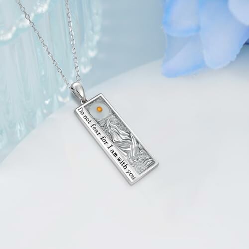 Silver necklace pendant with engraved text 'Do not fear for I am with you'.