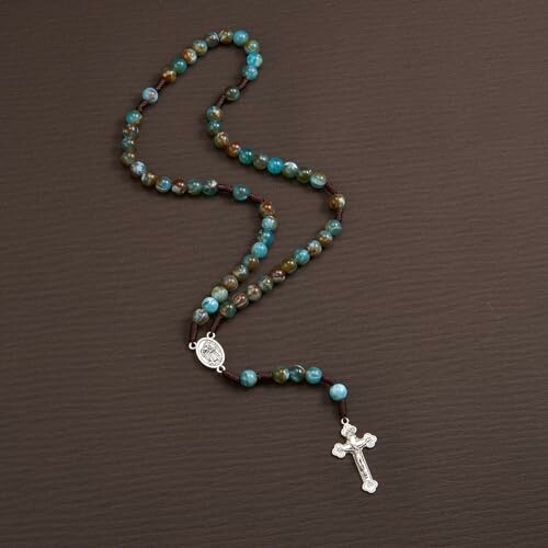 Turquoise rosary beads with a cross on a dark surface.