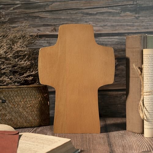 Wooden cross decoration on a rustic table with books and dried flowers.