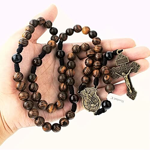 Hand holding a wooden rosary with beads and a cross.
