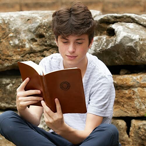 Young man reading a book outdoors by rocks